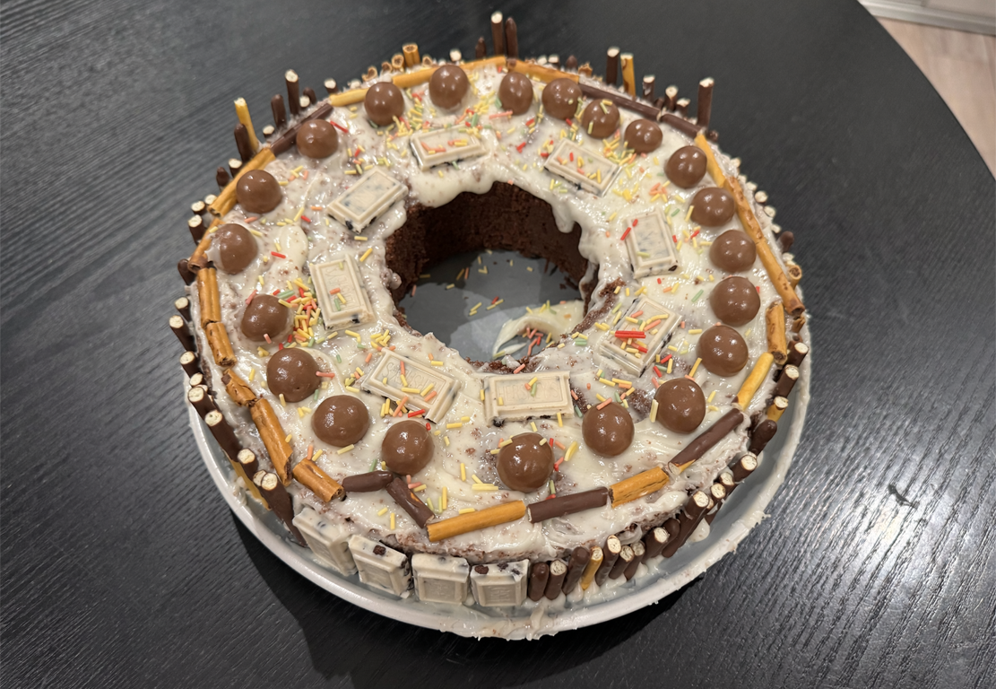 Birthday ring cake topped with chocolate balls, wafer sticks, chocolate bars and sprinkles.